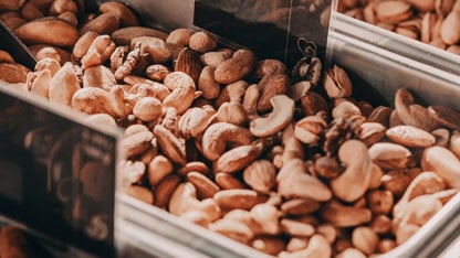 Un primer plano de una variedad de frutos secos, incluyendo anacardos, almendras y nueces, mostrados en un recipiente de metal.