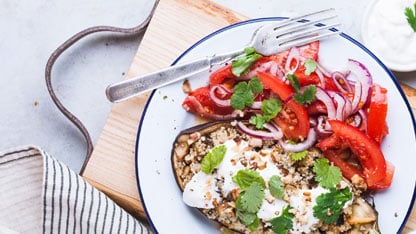 Plato saludable de comida con quinoa, berenjena, tomate, cebolla morada y cilantro.