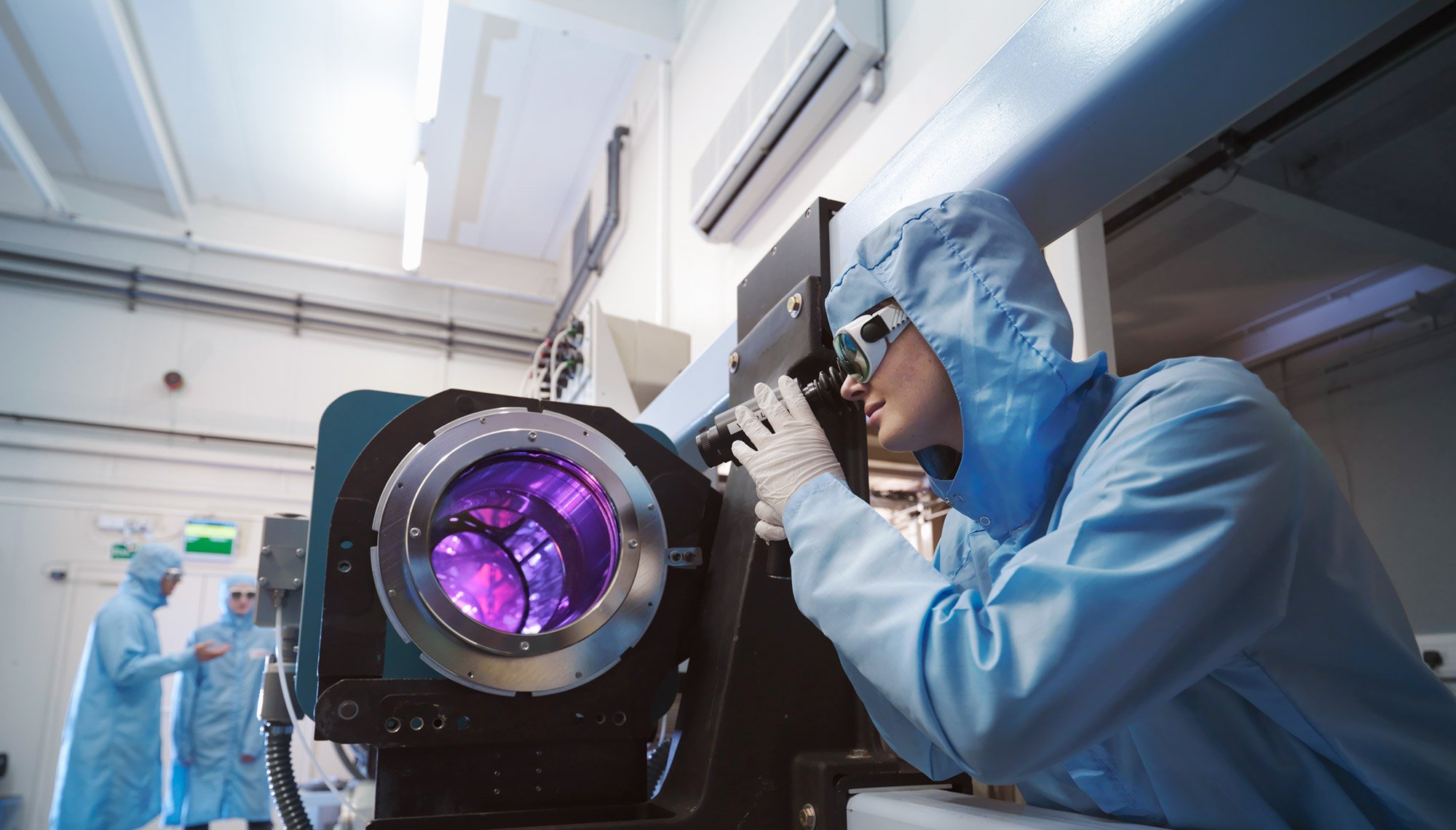 Científicos con ropa de protección y gafas en un laboratorio junto a equipos láser.