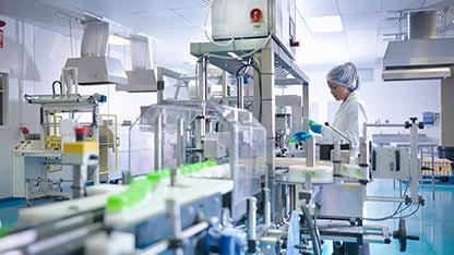 Trabajador inspeccionando productos en la línea de producción en una fábrica farmacéutica