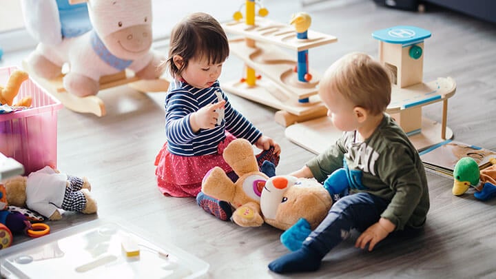 Dos niños juntos en un suelo con juguetes y peluches